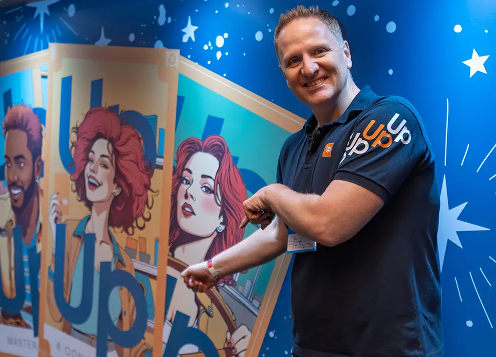 Thomas Pillet com uniforme da Up Brasil ao lado de painel ilustrado da marca durante evento corporativo